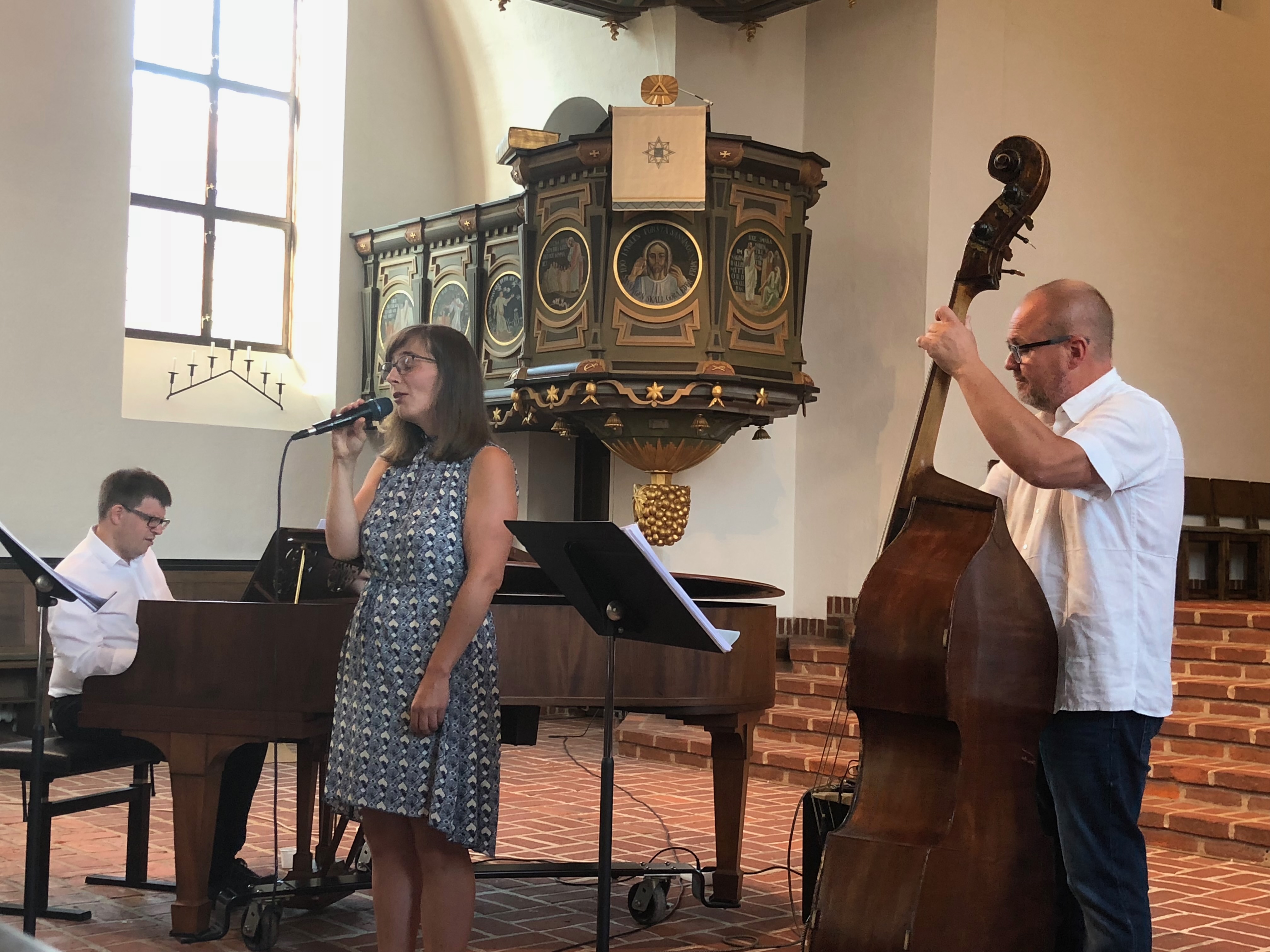 Julia sjunger i en ljus kyrka intill predikstolen, tillsammans med en pianist och en kontrabasist.